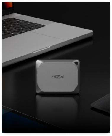 A Crucial X9 Pro 4TB Portable SSD set vertically on a desk in front of a laptop.